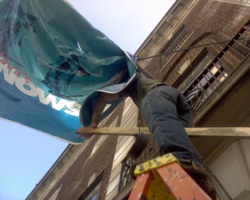 A man tries to hang a banner while standing on a ladder.